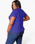 A woman modeling a short-sleeve royal purple top from the back, paired with blue jeans, against a clean white studio background.