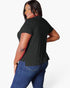 A woman modeling a black short-sleeve t-shirt from the back, paired with blue jeans, against a plain white studio background.