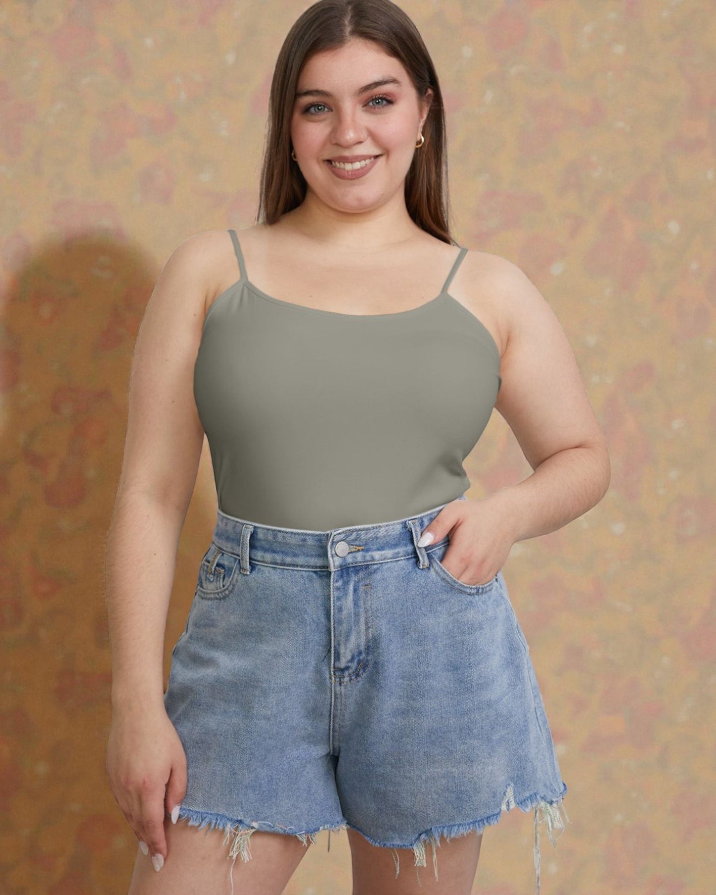 Woman wearing a green tank top and denim shorts against a patterned background