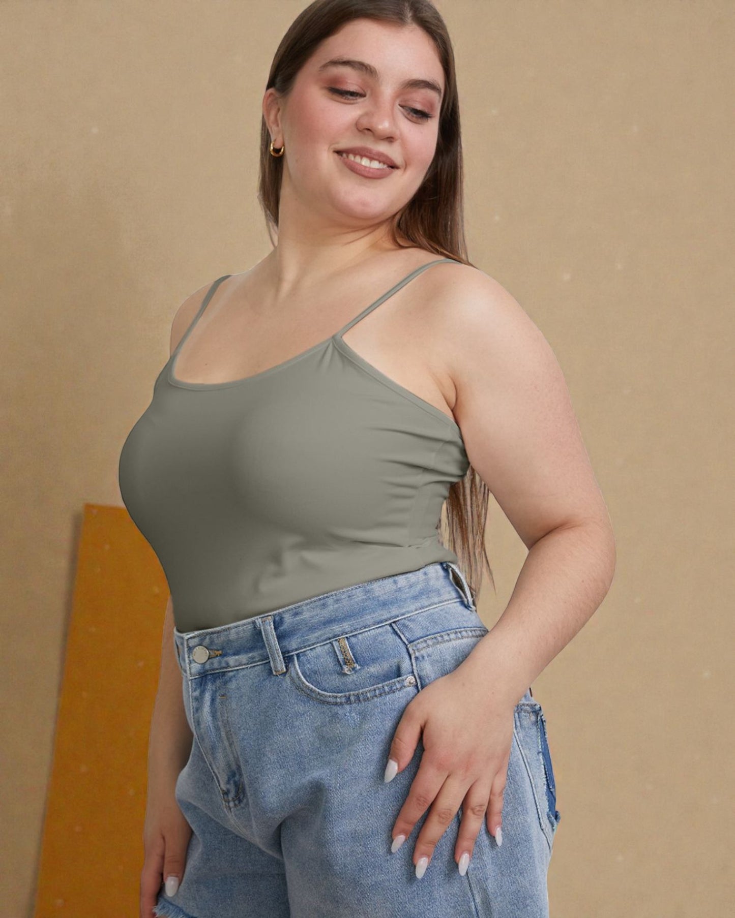 Woman wearing a green tank top and blue jeans against a beige background