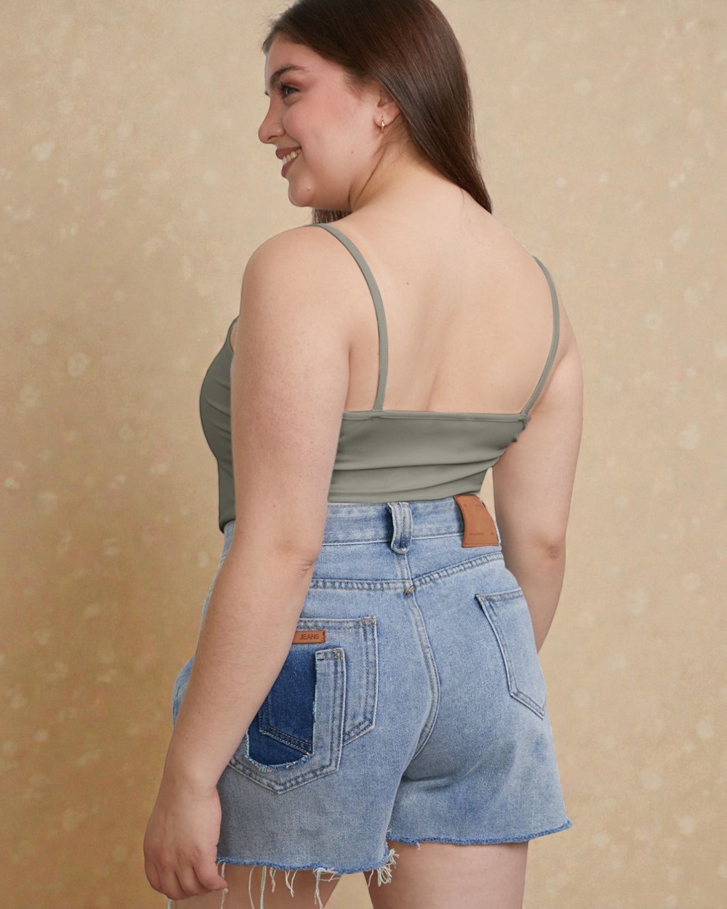 Woman wearing a green tank top and denim shorts against a beige background