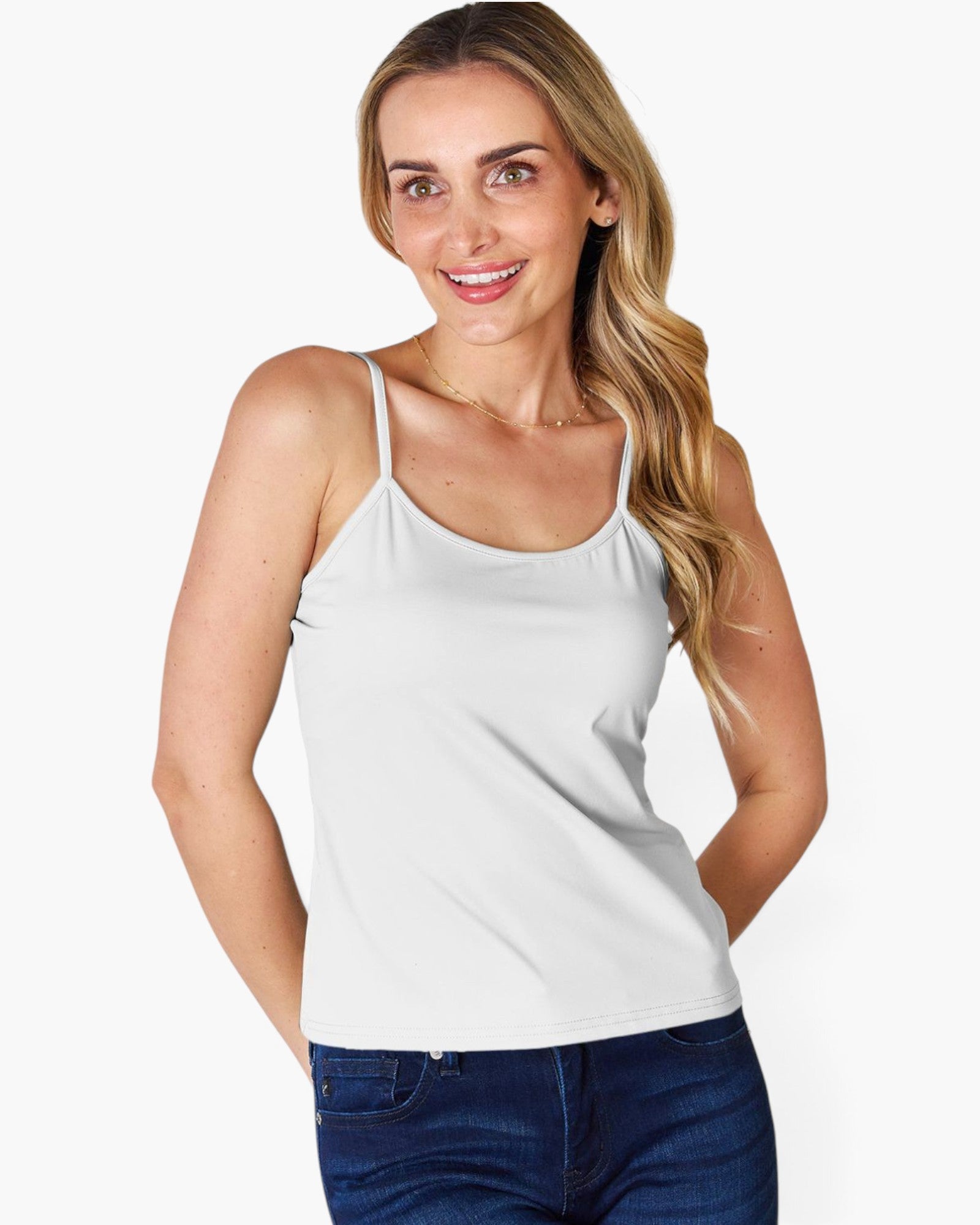 A woman modeling a white spaghetti-strap tank top paired with dark blue jeans, set against a plain light gray studio background.