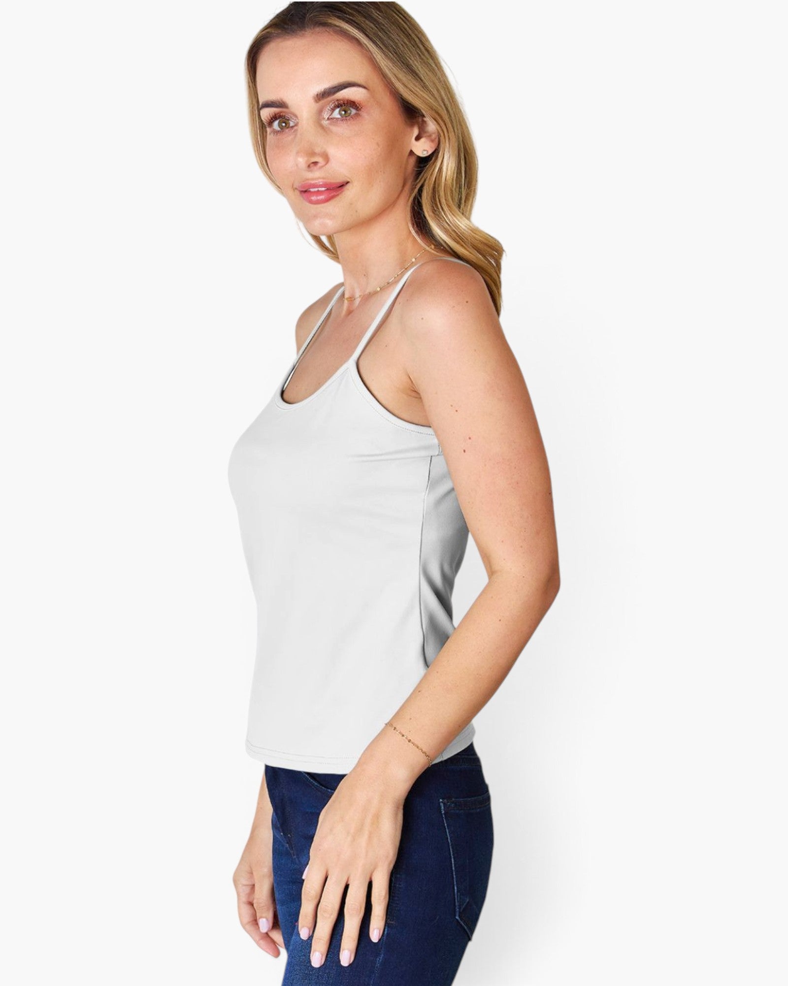 A woman modeling a light gray sleeveless camisole tank top with thin straps, paired with dark blue jeans, against a plain white background.