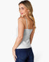 A woman with blonde hair is shown from the back wearing a light gray spaghetti-strap camisole top and dark blue jeans, set against a plain white studio background.