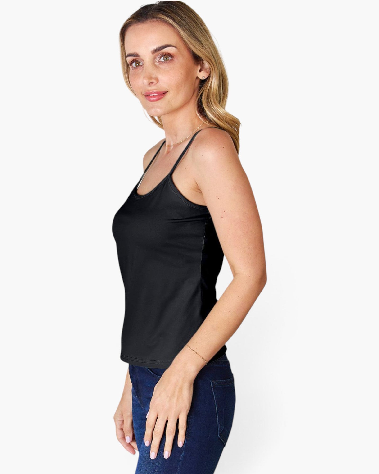 A woman modeling a black spaghetti-strap tank top paired with dark blue jeans, photographed against a clean white studio background.