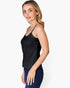 A woman modeling a black spaghetti-strap tank top paired with dark blue jeans, photographed against a clean white studio background.
