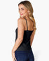 A woman with blonde hair is shown from the back wearing a black spaghetti-strap camisole top and dark blue jeans against a light gray studio background.