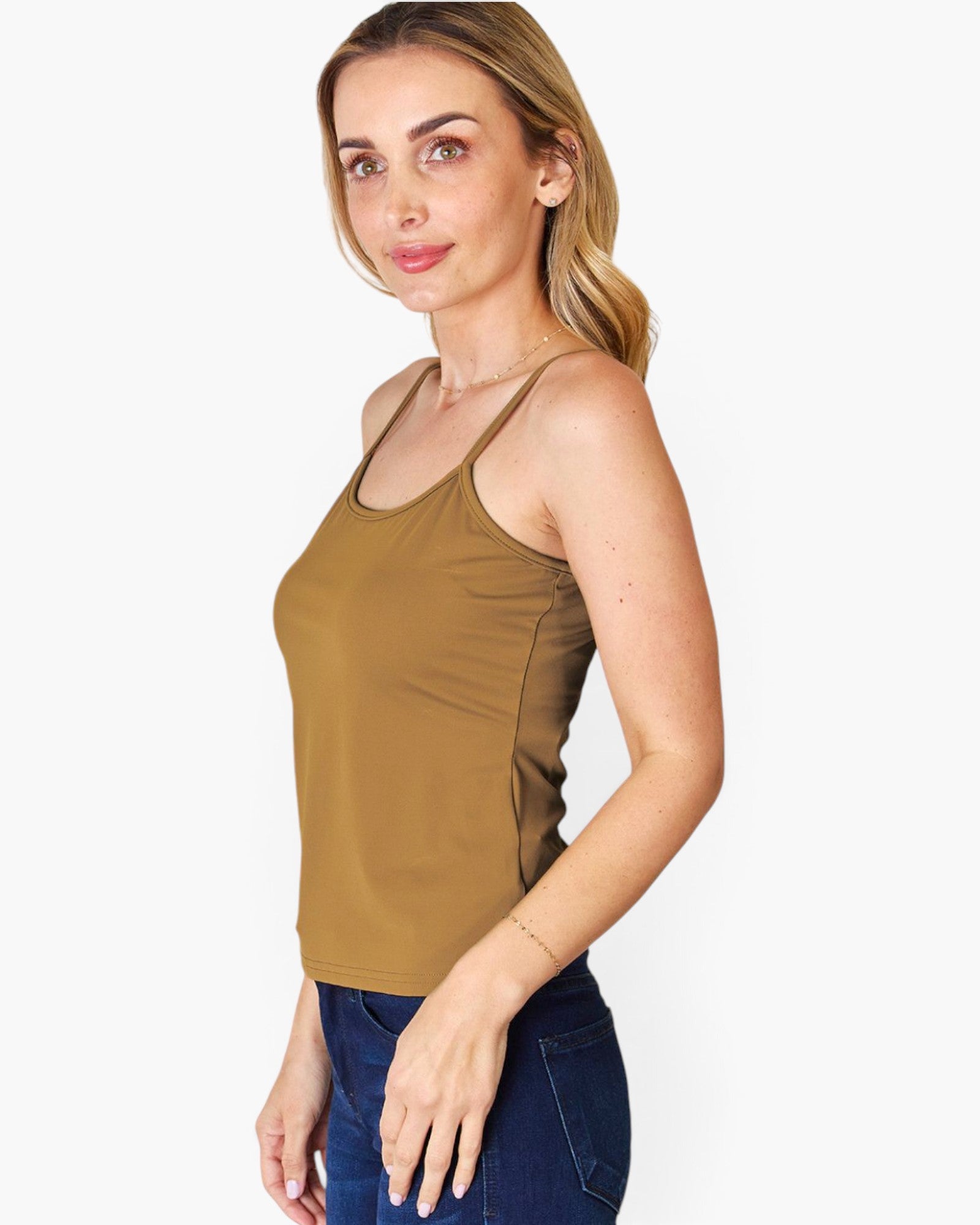 A woman wearing a fitted tan-brown tank top and dark blue jeans, shown from the waist up against a plain light gray studio background.