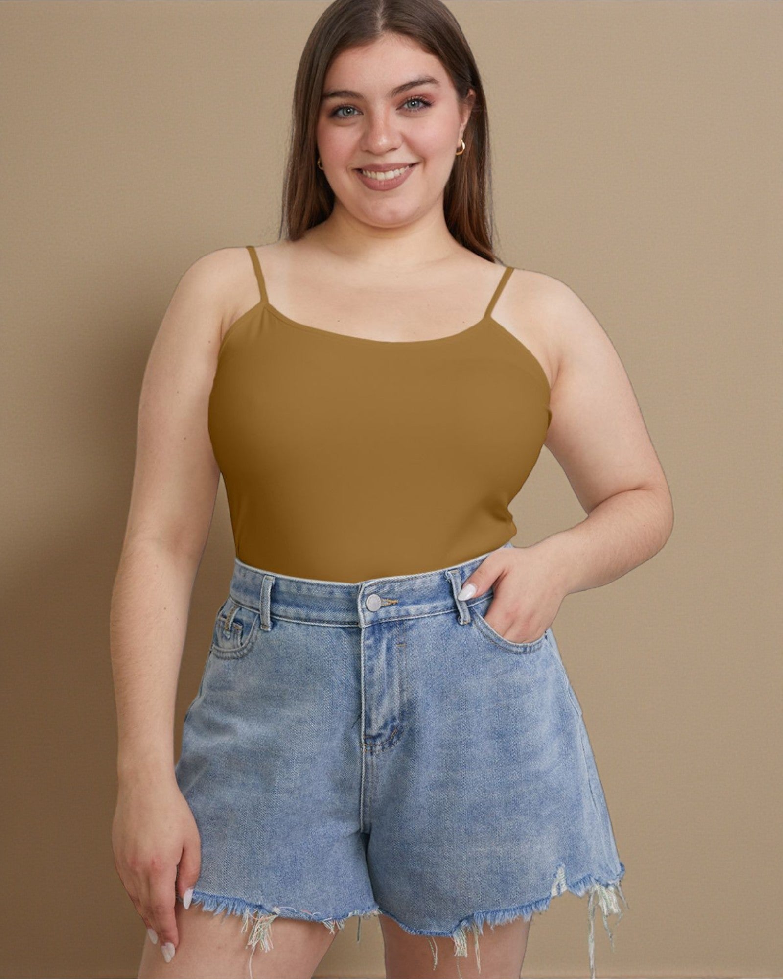 Woman wearing a mustard yellow tank top and denim shorts against a beige background