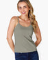A woman wearing a light sage green spaghetti-strap tank top and dark blue jeans, standing against a plain white background.