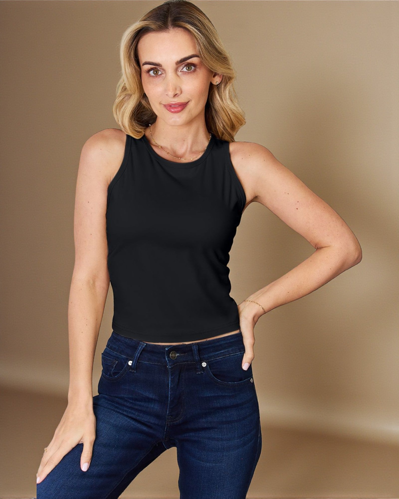 Woman wearing a black sleeveless top and blue jeans against a beige background