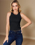 Woman wearing a black sleeveless top and blue jeans against a beige background