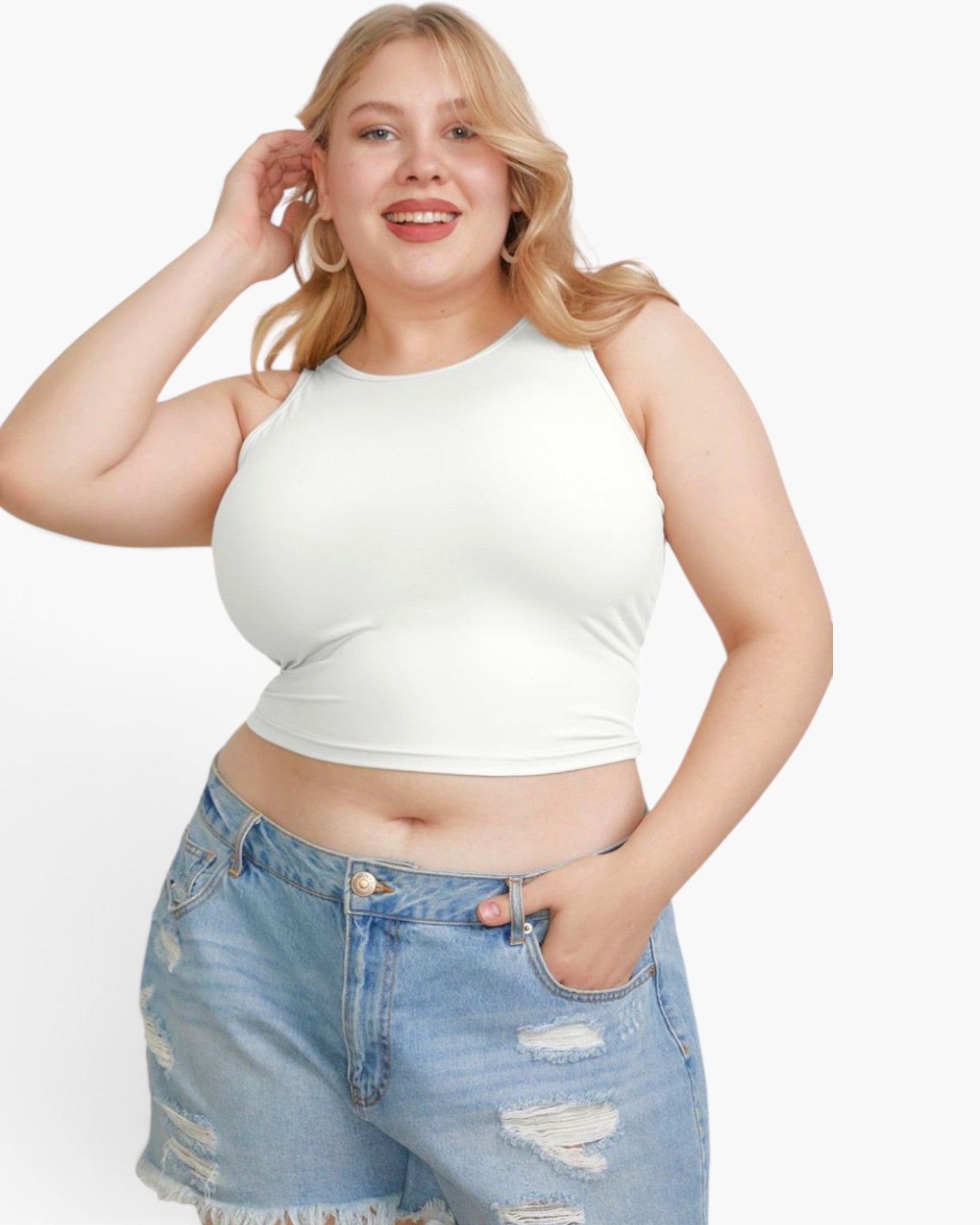 A plus-size blonde woman wearing a fitted white sleeveless crop top and light blue distressed denim shorts, posing against a light gray studio background.