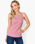A woman modeling a sleeveless dusty pink tank top paired with dark blue jeans, photographed against a clean white studio background.