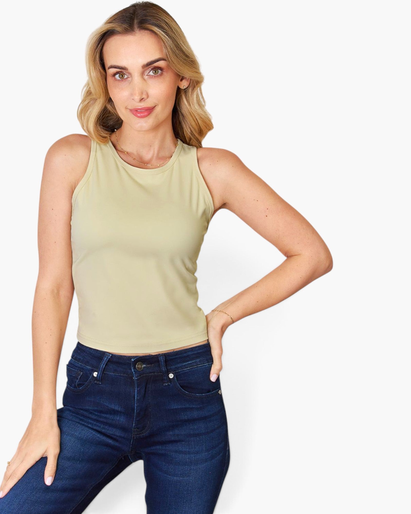 A woman modeling a sleeveless light beige tank top paired with dark blue jeans, set against a plain light gray background.