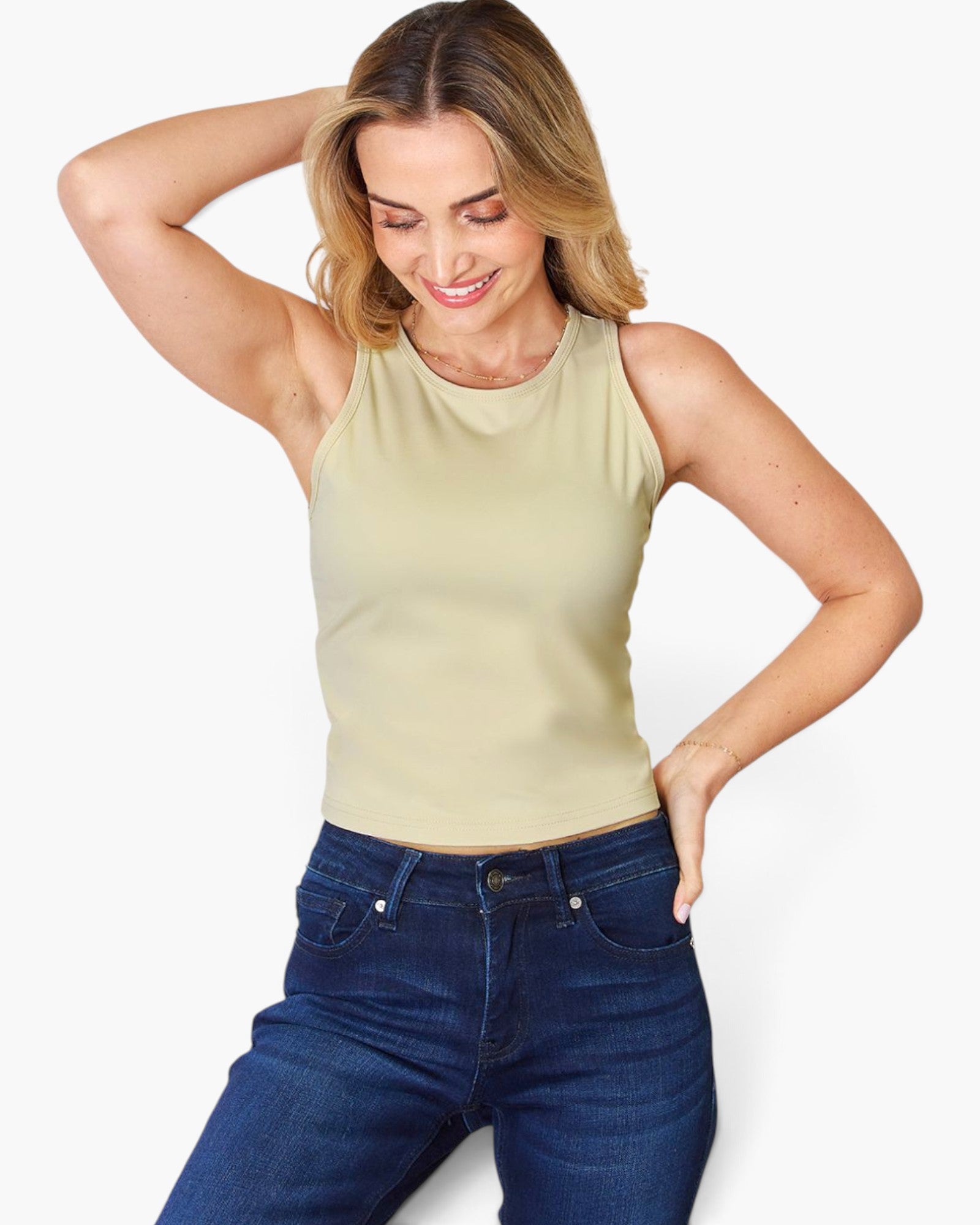 A woman wearing a sleeveless light beige tank top and dark blue jeans, posing against a clean white background.