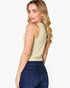 A woman with blonde wavy hair is shown from the back wearing a light beige sleeveless tank top and dark blue jeans against a plain white background.