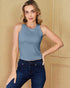 Woman wearing a blue sleeveless top and dark jeans against a beige wall.