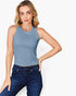 A woman modeling a sleeveless, scoop-neck crop top in a dusty slate blue color, paired with dark blue jeans, against a plain light gray background.