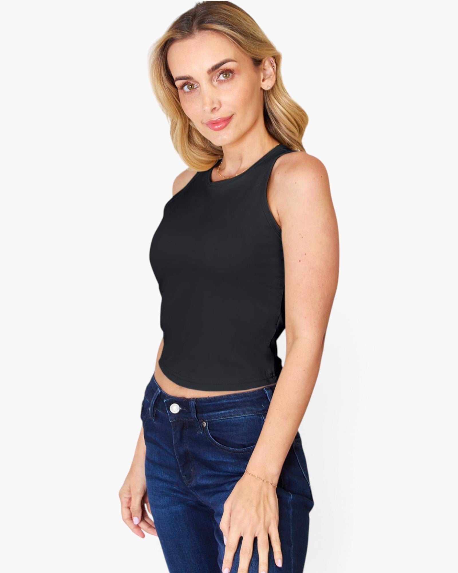 A woman modeling a black sleeveless crop top paired with dark blue jeans, photographed against a clean light gray studio background.