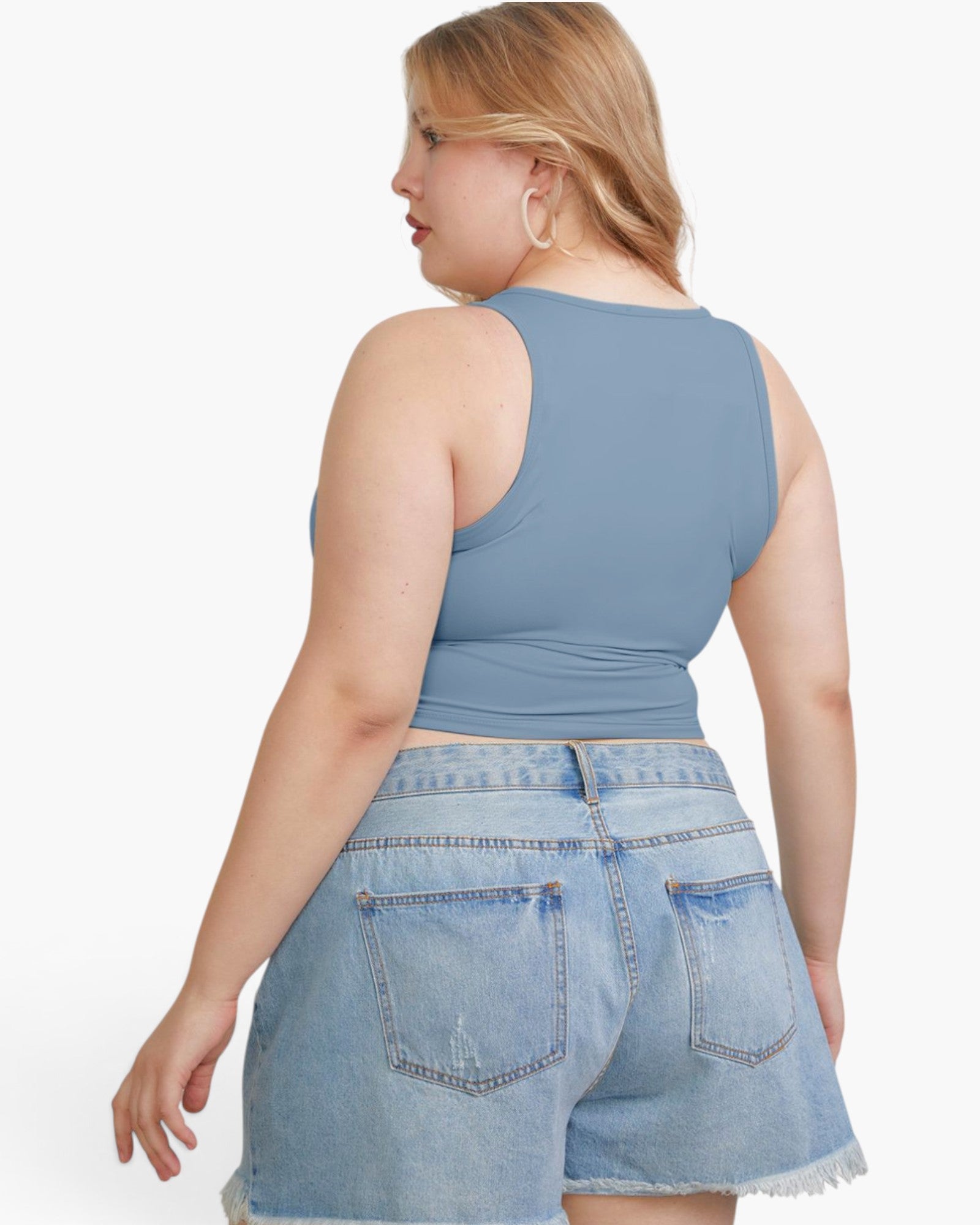 A woman shown from the back wearing a dusty blue sleeveless crop top and light-wash denim shorts against a plain white studio background.