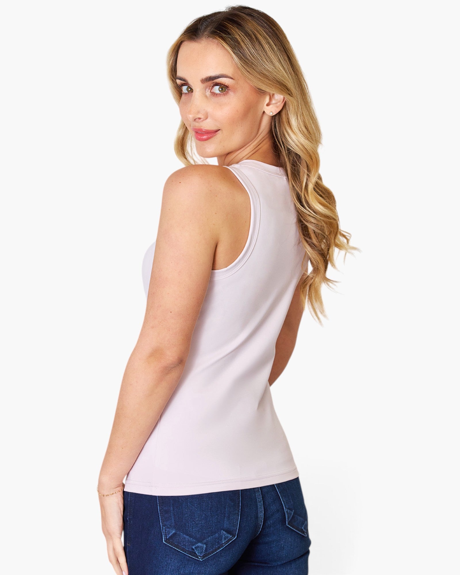 A woman wearing a light pink sleeveless tank top and dark blue jeans, photographed from the back against a plain white studio background.