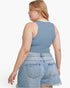 A woman shown from the back wearing a dusty blue sleeveless crop top and light-wash denim shorts against a plain white studio background.