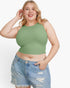 A plus-size blonde woman wearing a sage green ribbed halter crop top and light-wash distressed denim shorts, posing against a solid white studio background.