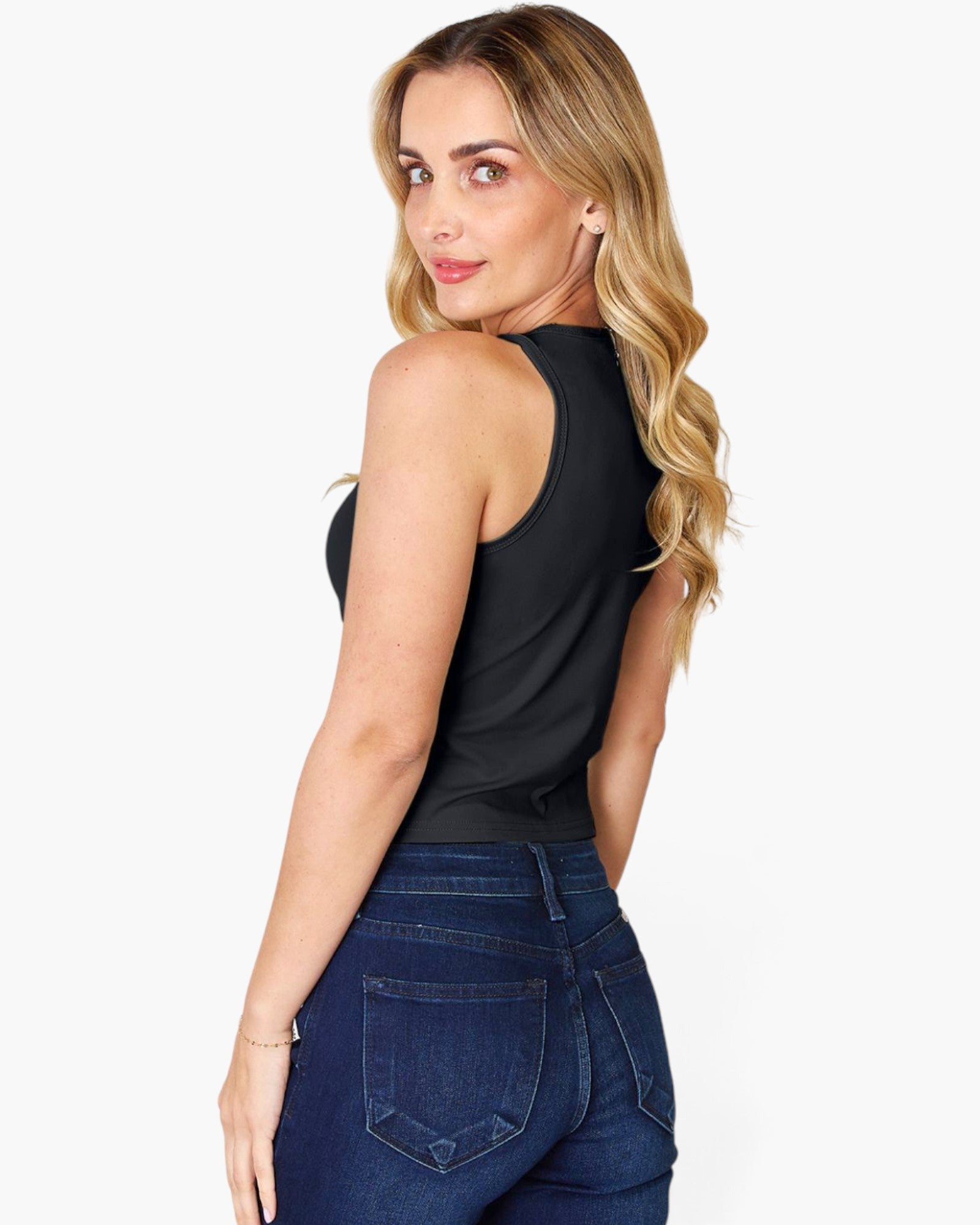 A woman wearing a black sleeveless tank top and dark blue jeans, photographed from the back against a light gray studio background.