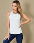 Woman wearing a white sleeveless top and blue jeans against a beige background