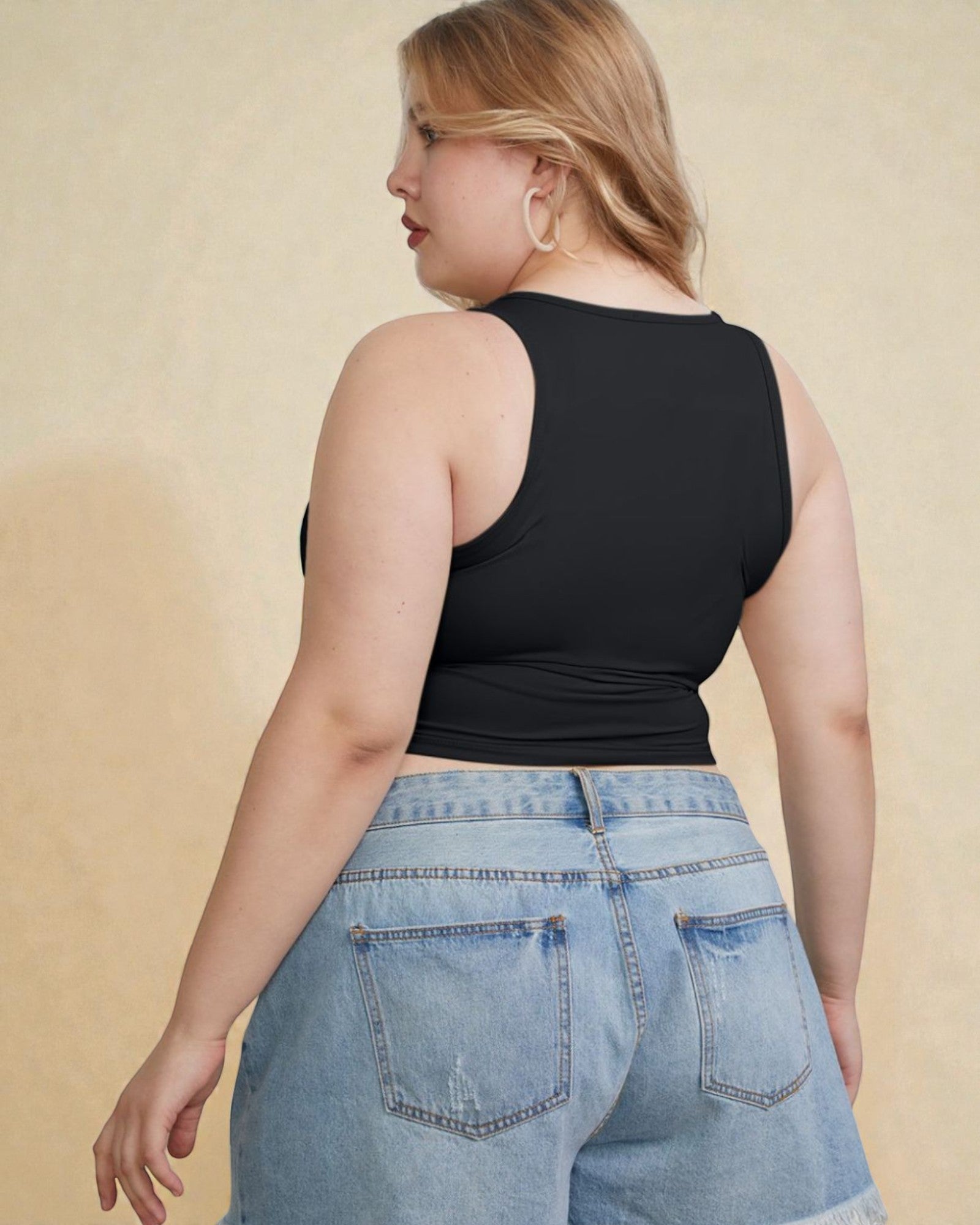 Woman wearing a black tank top and blue jeans against a beige background