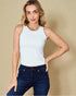 Woman wearing a white sleeveless top and dark blue jeans against a beige background