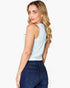 A woman with blonde wavy hair is shown from a back-three-quarter angle wearing a light blue ribbed tank top and dark blue jeans against a plain white background.