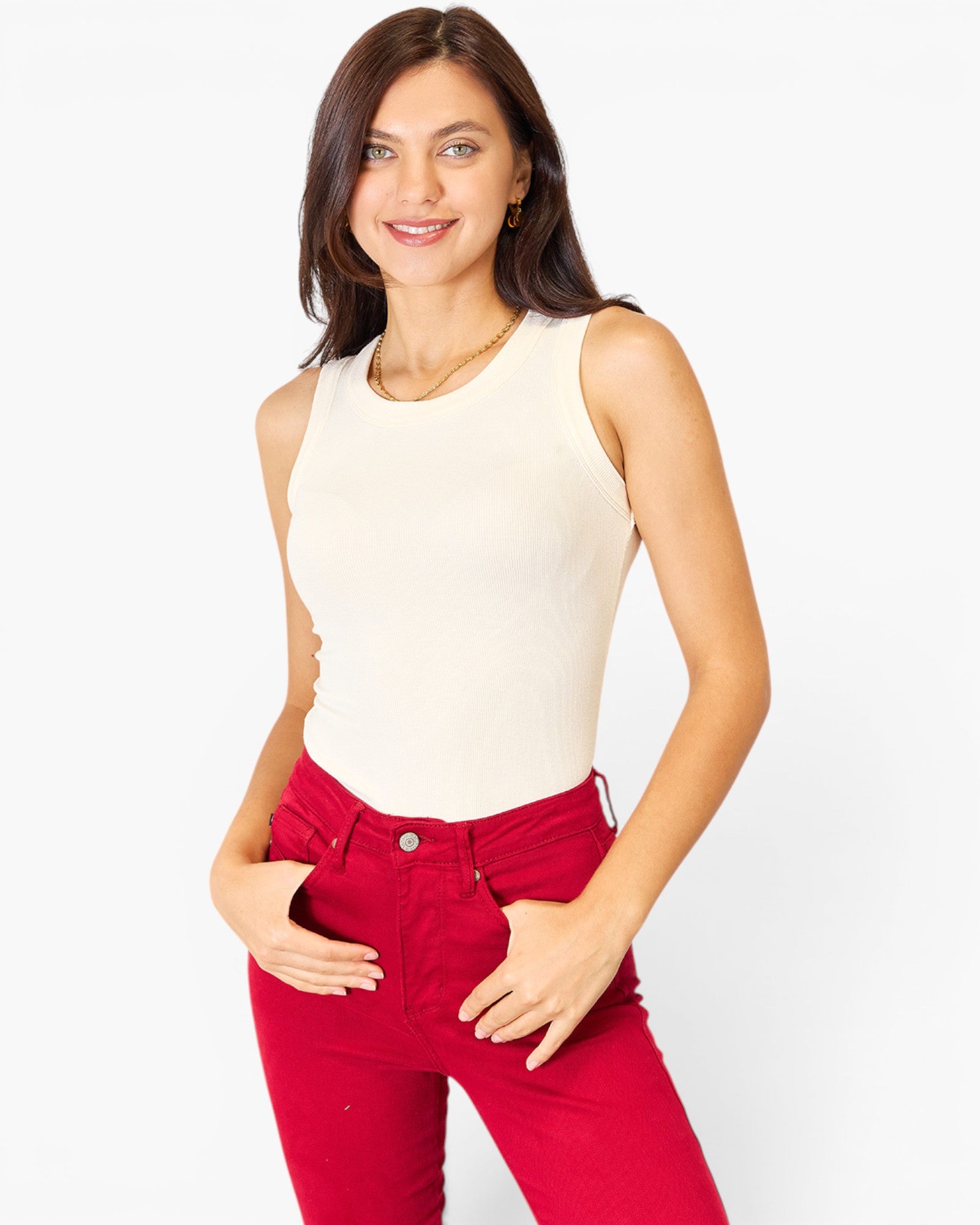 A woman modeling a sleeveless cream ribbed tank top paired with bright red jeans, set against a plain white studio background.