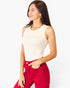 A woman wearing a fitted sleeveless cream top and bright red jeans, photographed against a clean light gray studio background.