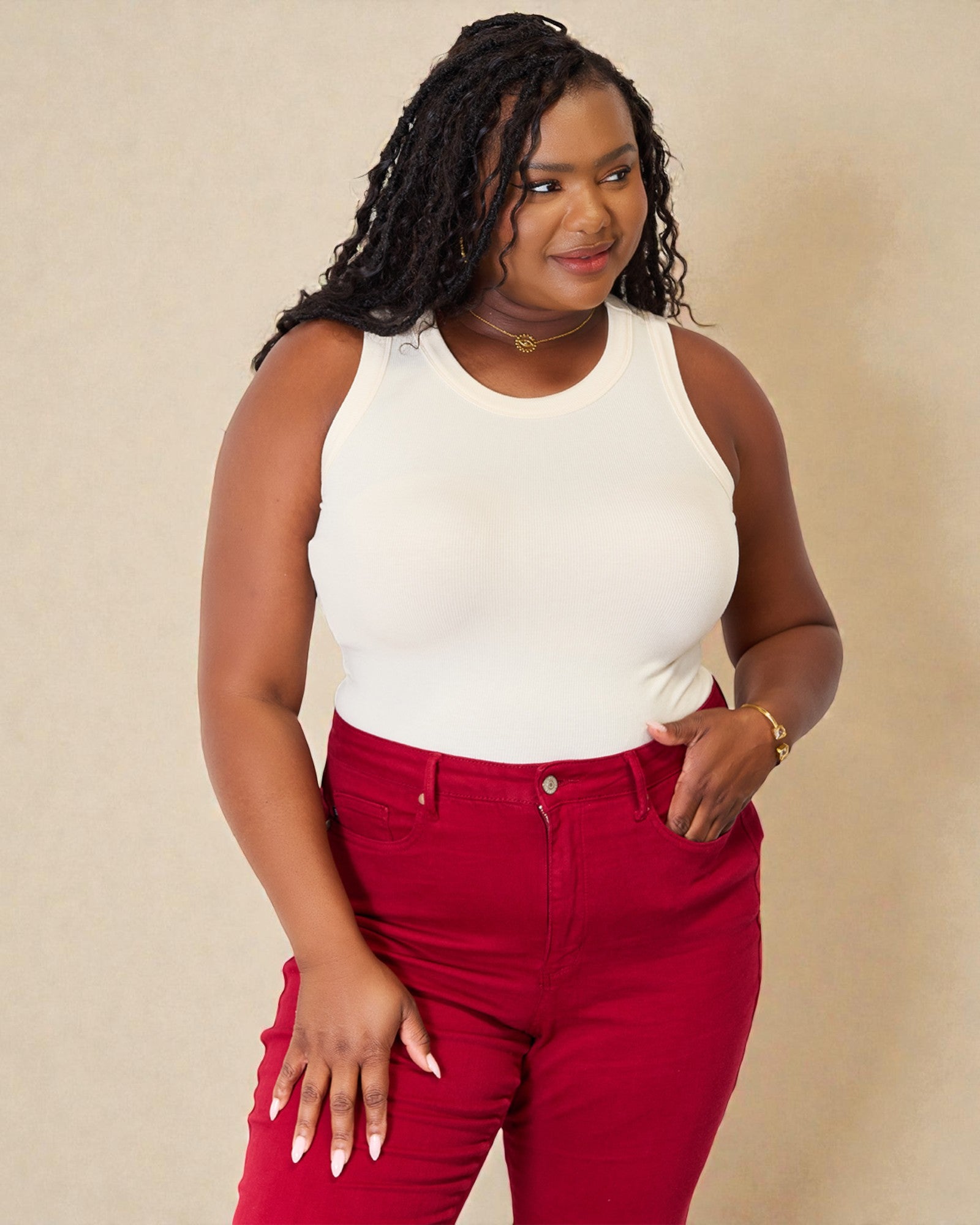 Woman wearing a white sleeveless top and red pants against a beige background