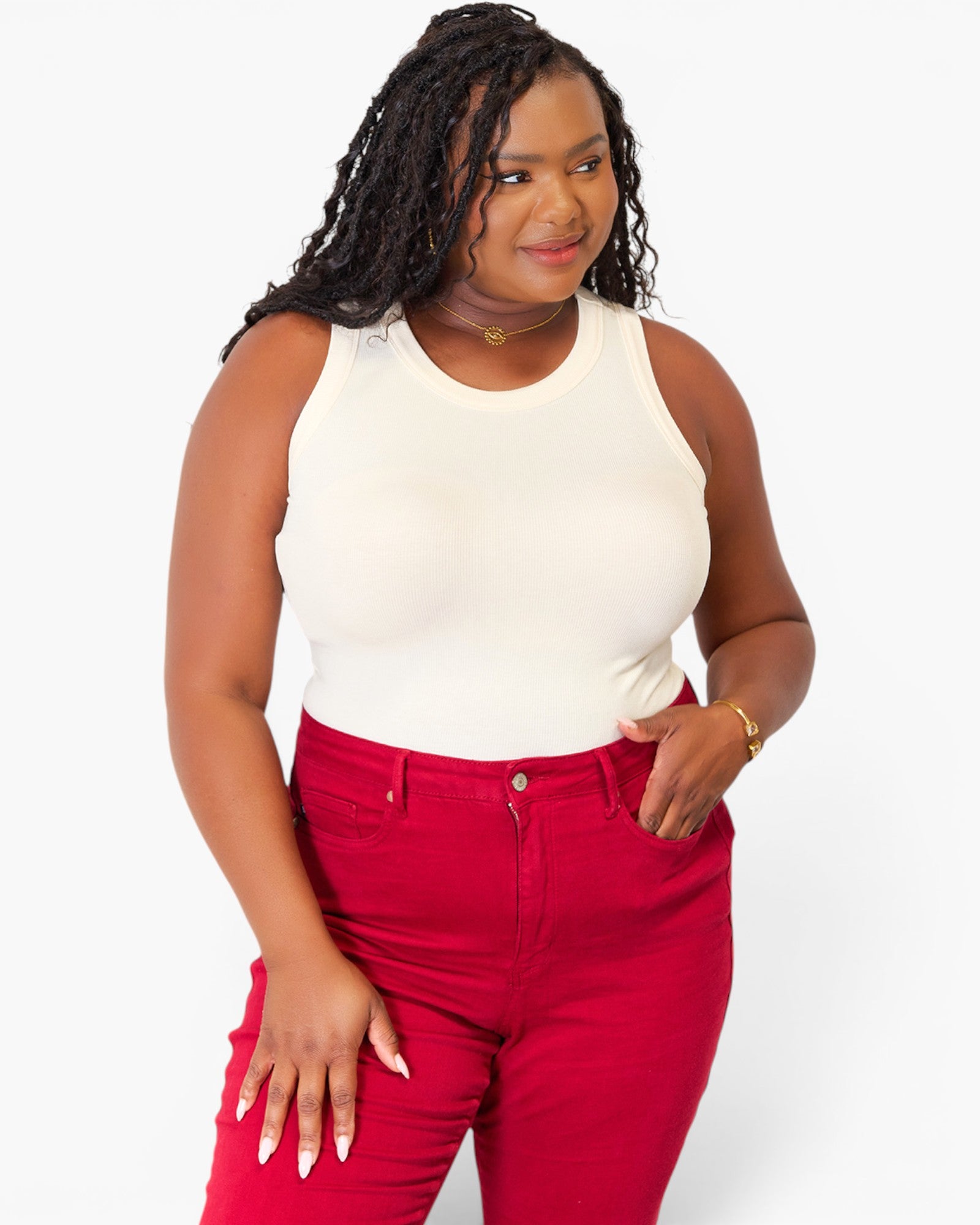 A woman modeling a sleeveless cream top and bright red pants against a plain light gray studio background.