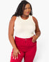 A woman modeling a sleeveless cream top and bright red pants against a plain light gray studio background.
