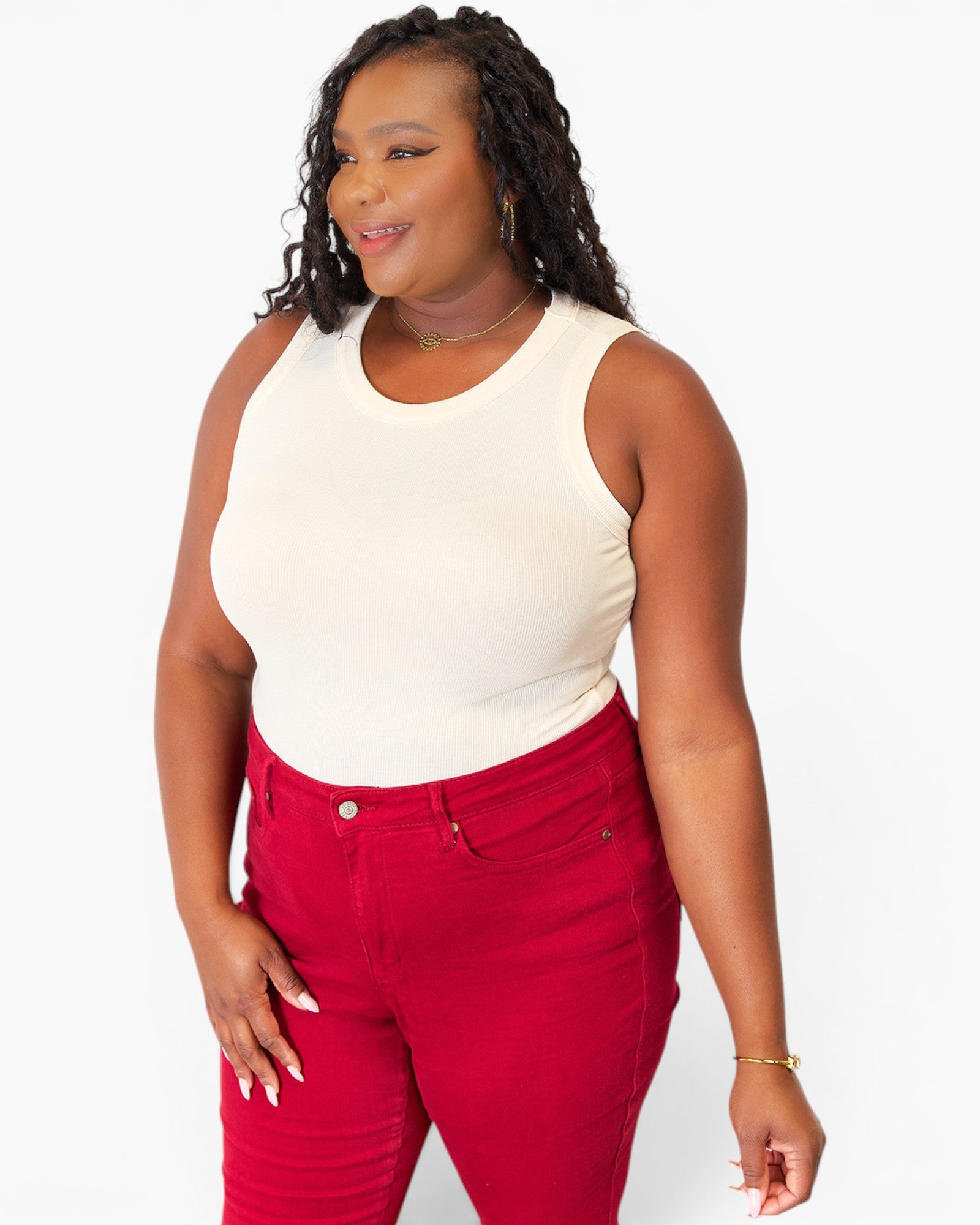 A woman modeling a sleeveless cream top and bright red pants against a plain light gray studio background.