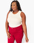 A woman modeling a sleeveless cream top and bright red pants against a plain light gray studio background.