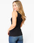 A woman with long blonde wavy hair is shown from a side-back angle wearing a fitted black sleeveless tank top and blue jeans against a plain light gray studio background.