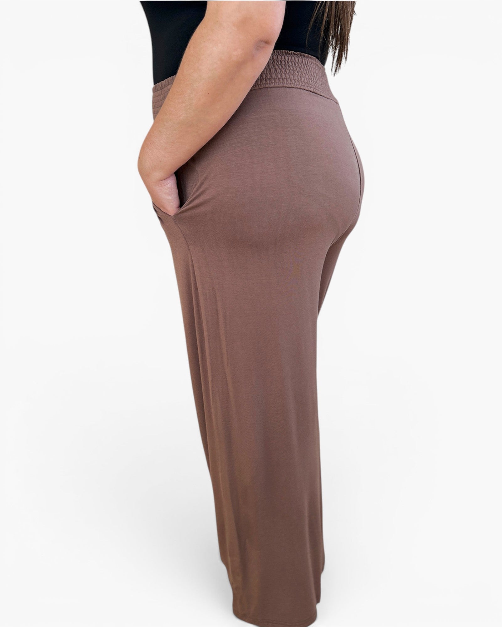 A side view of a person wearing a pair of high-waisted, wide-leg knit pants in a muted taupe-brown color, with a black top partially visible.