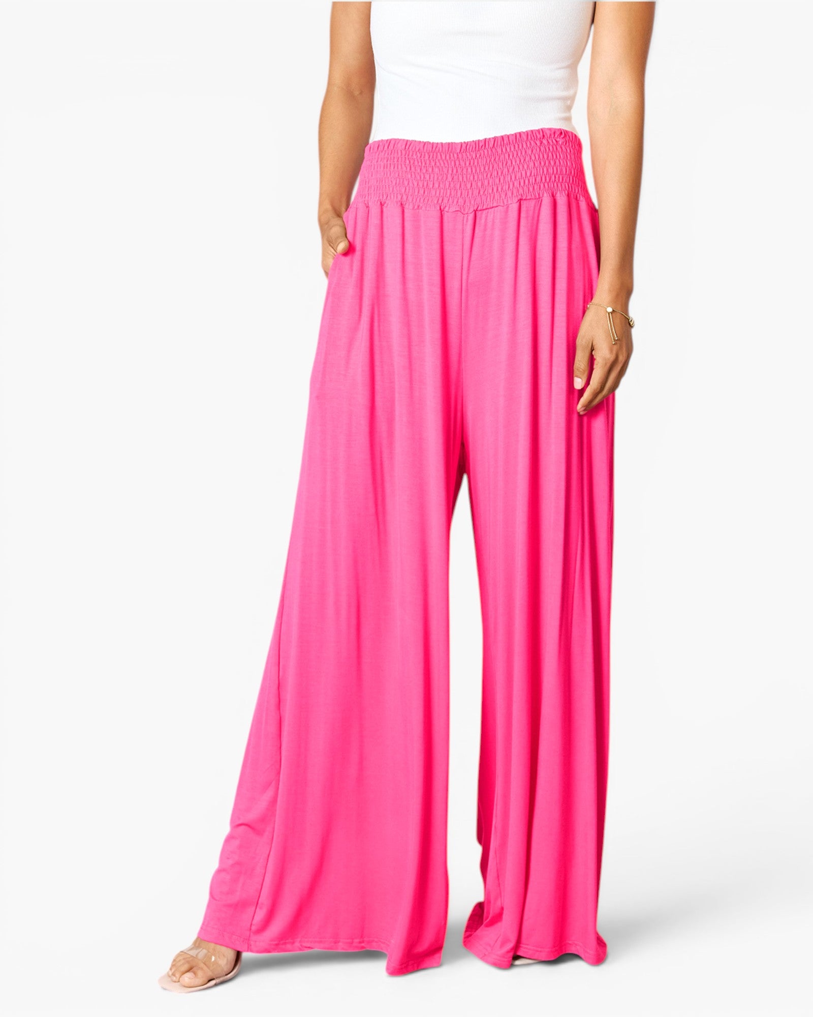 Bright pink wide-leg pants with a smocked elastic waistband, shown on a model wearing a white top against a light gray studio background.