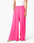 Bright pink wide-leg pants with a smocked elastic waistband, shown on a model wearing a white top against a light gray studio background.
