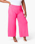 Bright pink wide-leg cropped pants worn by a model, paired with a white top and clear high-heel sandals, against a clean white studio background.