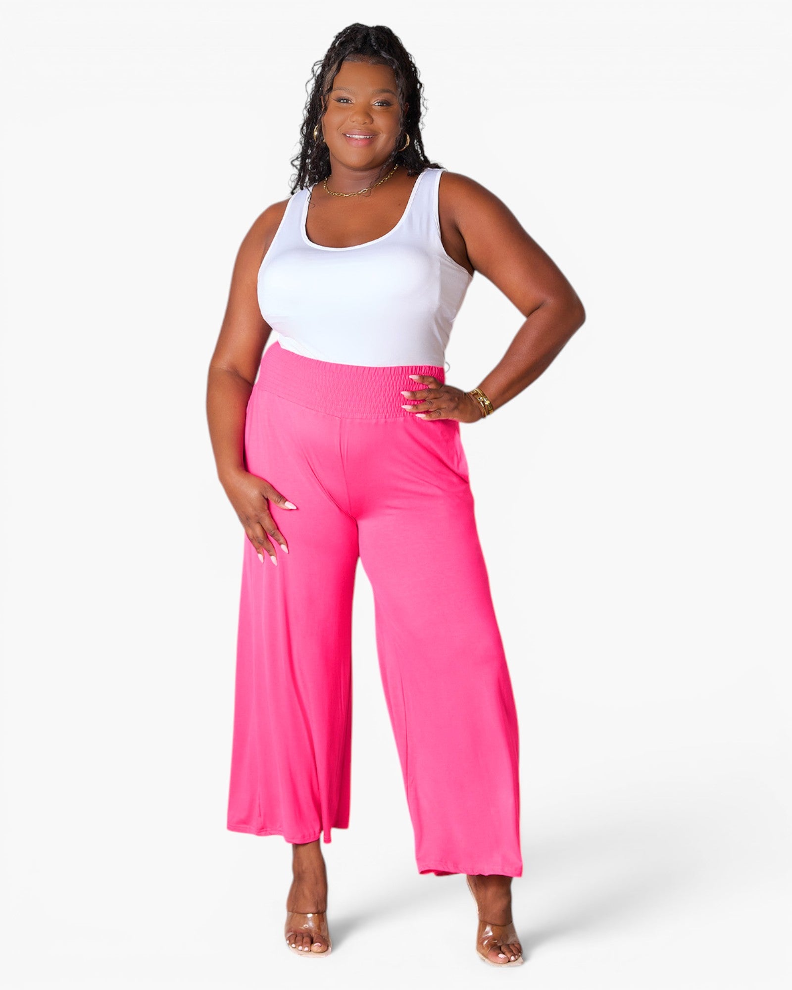 A woman modeling bright pink wide-leg cropped pants with a white tank top, standing against a light gray studio background.