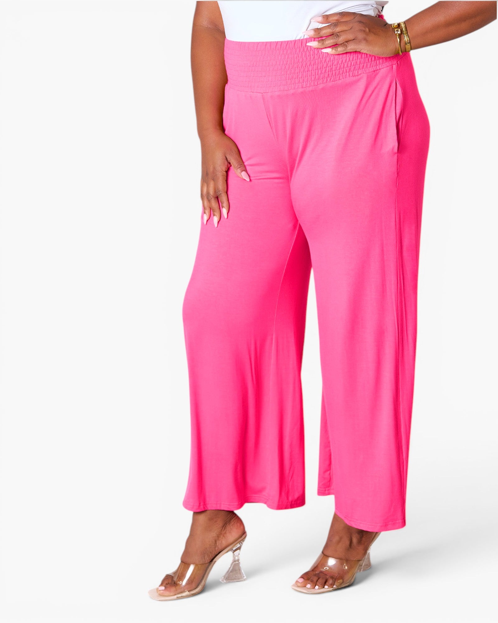 Bright pink wide-leg cropped pants worn by a model, paired with a white top and clear high-heel sandals, against a clean white studio background.