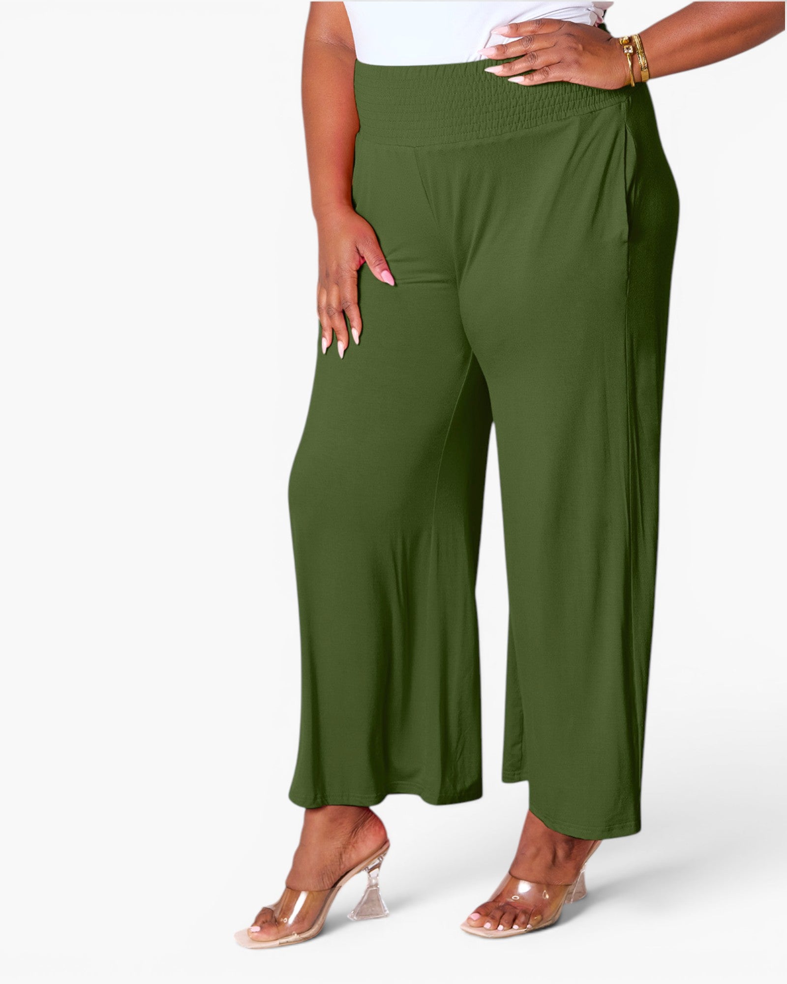 A model wearing olive green wide-leg cropped pants with a smocked elastic waistband, paired with clear high-heeled sandals, shown against a plain white studio background.
