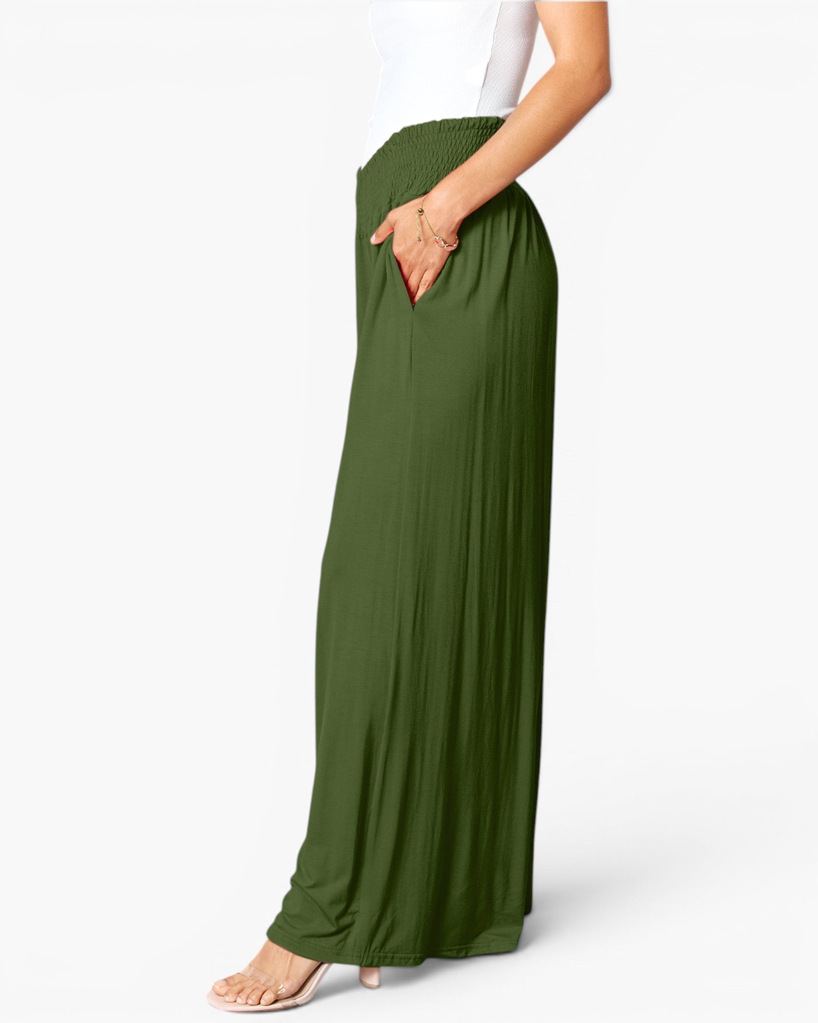 A model wearing olive green wide-leg pleated maxi pants with side pockets, paired with a white top and beige high-heeled sandals, shown from the waist down against a light gray studio background.