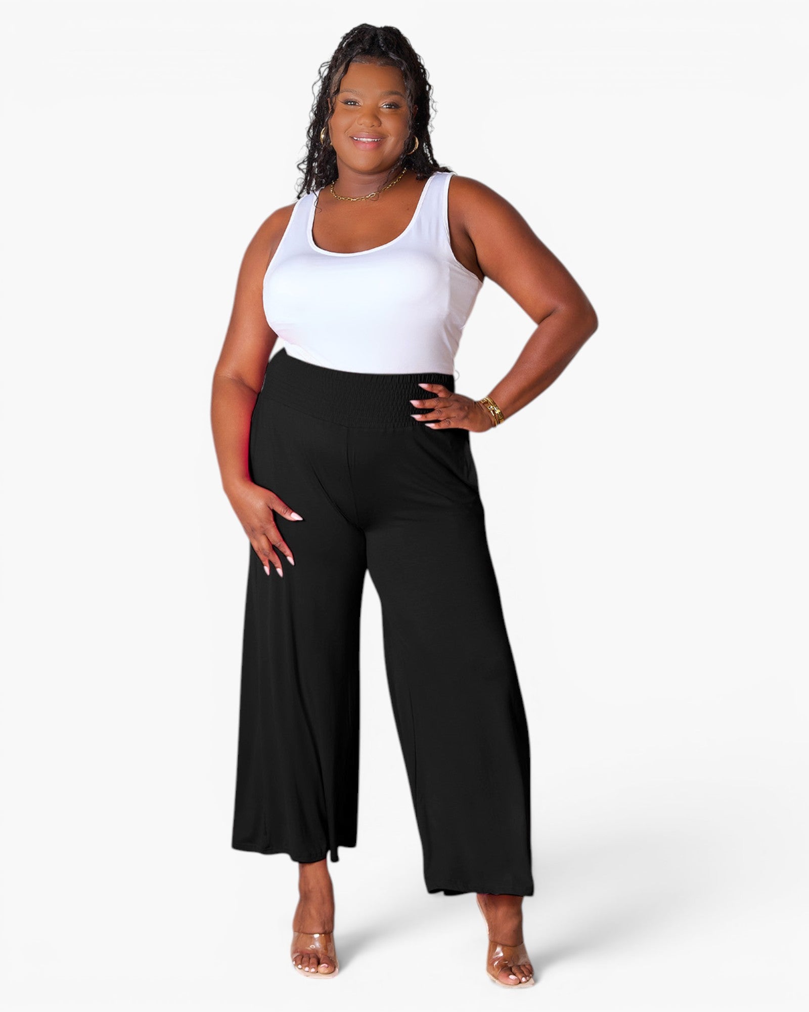 A woman modeling black wide-leg cropped pants with a white ribbed tank top, standing against a plain white studio background.